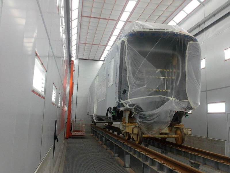 Rail car inside a large paint booth with overhead lighting.