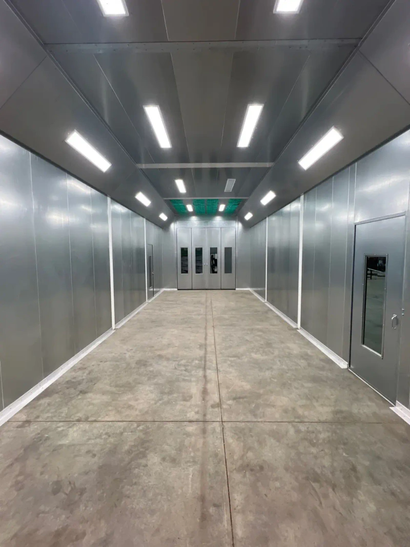 Large equipment paint booth with bright white interior and blue doors.