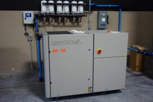 Compresor de aire industrial Mattei AC 18 con tuberías azules conectadas en un taller.