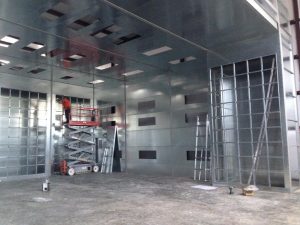 Industrial paint booth installation with worker on scissor lift inside metal chamber