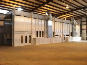 Large industrial paint booth inside a spacious warehouse with metal vents and multiple entry doors