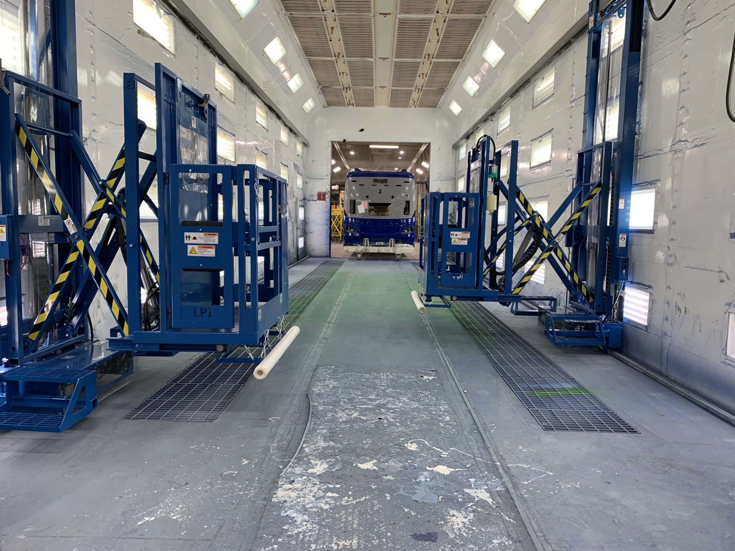 Spacious industrial paint booth with blue lift equipment.