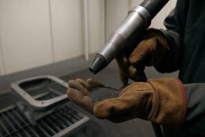 Gloved hands holding abrasive media with spray equipment in industrial paint booth